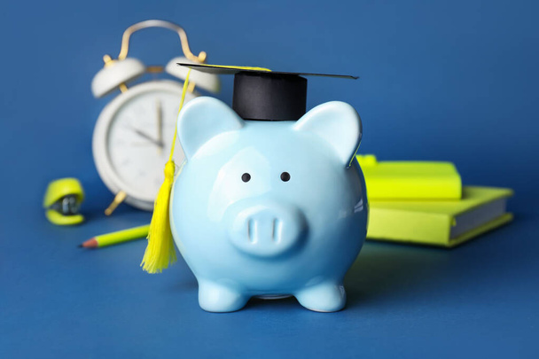 Hucha con sombrero de graduación, papelería y despertador en el fondo de color - Foto, imagen