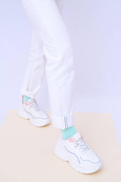 Details of trendy casual spring summer outfit. Girl in studio wearing white jeans and stylish  sneakers. Everyday look. Street fashion concept. No face. Minimalist aesthetic. - Foto, Imagen