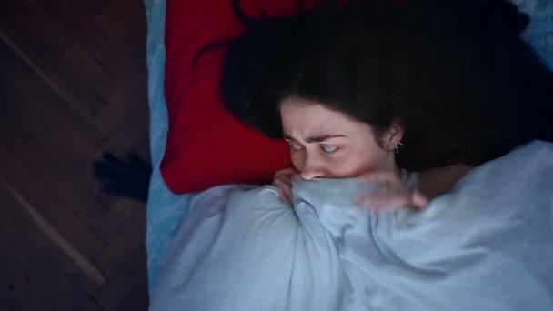 Eine junge Frau liegt erschrocken im Bett, nachdem sie etwas Beängstigendes gesehen hat und versteckt sich unter einer Decke vor einem Bettmonster. Der Blick von oben. Das Konzept der Schlaflosigkeit und Albträume - Filmmaterial, Video