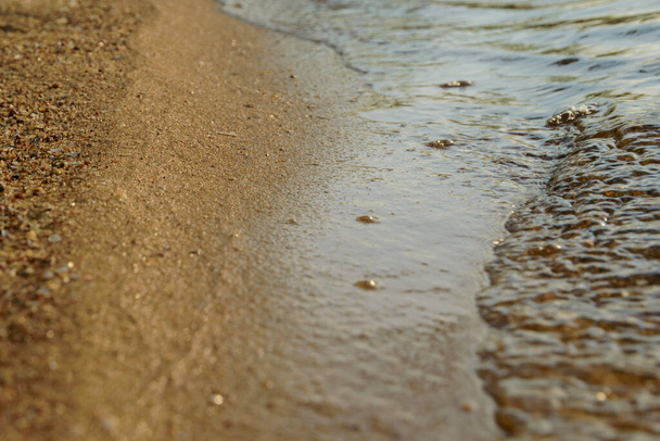 modrá vlna se blíží k okraji písku, břeh oddělující zrna od kamenů - Fotografie, Obrázek
