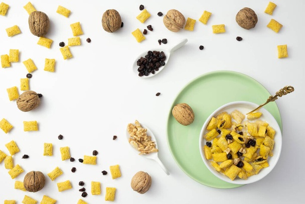 cornflakes, raisins and muesli in a plate for breakfast, near walnuts on a table on a white background - Photo, Image