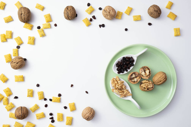 raisins and cornflakes are scattered on the table, near walnuts on a white background - Photo, Image