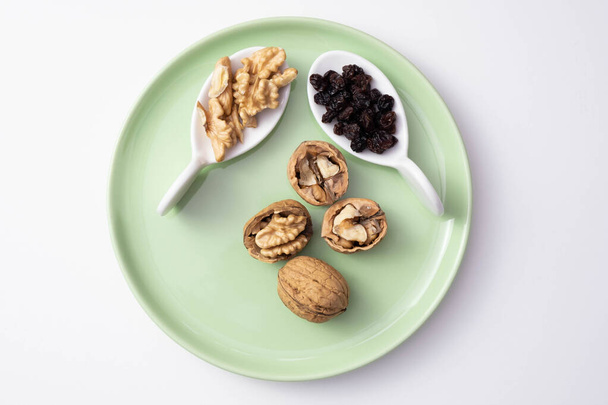 walnuts and raisins lie on a green plate, on a white background - Photo, Image