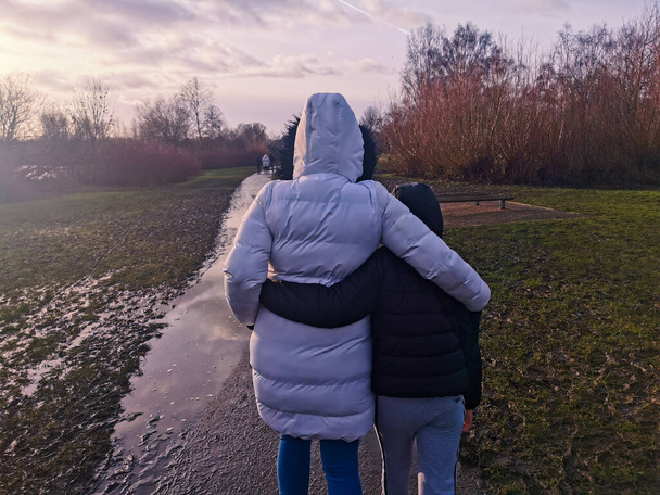 Maman et son fils s'embrassent en marchant dans un parc après qu'il ait été inondé par une journée froide. - Photo, image