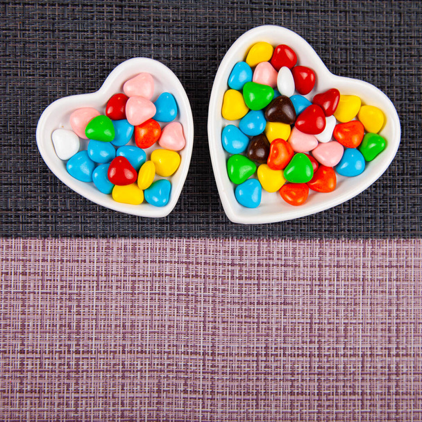 Multicolored candies in a heart-shaped plate on a black and pink background. Valentine's Day. Place for your text. - Foto, immagini