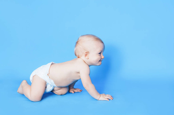 Een klein kind kruipt op een blauwe achtergrond. Zorgen voor de gezondheid van jonge kinderen. - Foto, afbeelding