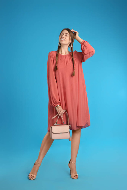 Beautiful young woman with stylish pink bag on light blue background - Foto, imagen