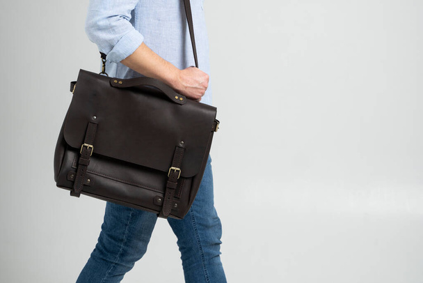 Brown mens shoulder leather bag for a documents and laptop on the shoulders of a man in a blue shirt and jeans with a white background. Satchel, mens leather handmade briefcase. - Foto, immagini