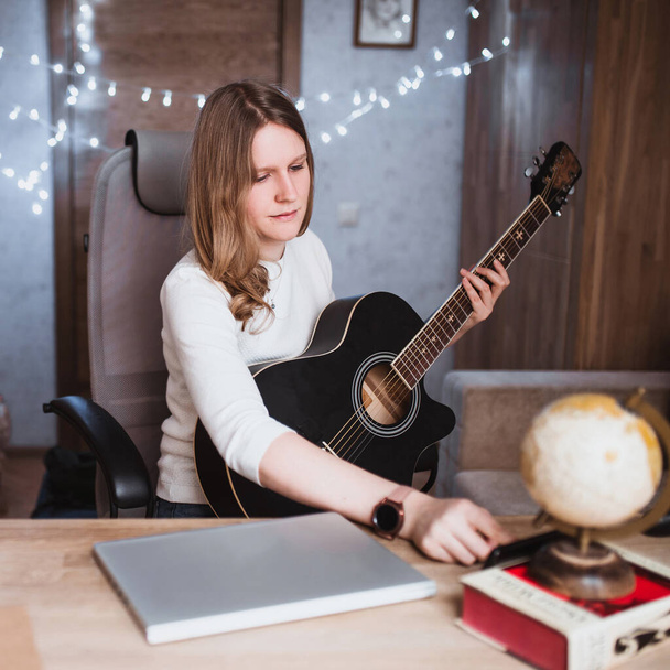 Blonde caucasian girl remotely learns to play the guitar - online music tutor training - Foto, Imagen