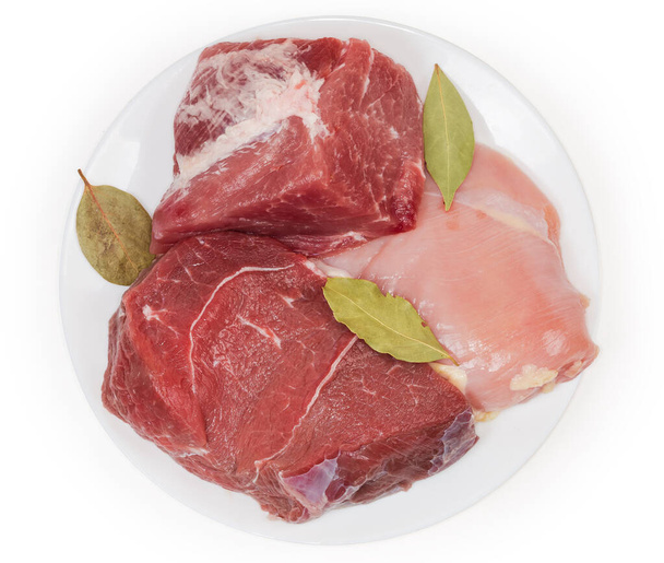 大きな片の骨のない豚肉と後ろ足の牛肉、白い背景に白い皿の上にベイリーフと鶏の胸肉、トップビュー - 写真・画像