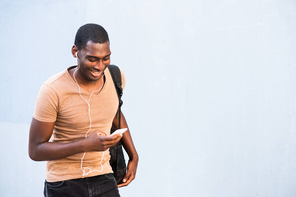 Портрет усміхненого молодого чорного чоловіка, який слухає музику зі смартфоном та навушниками
 - Фото, зображення