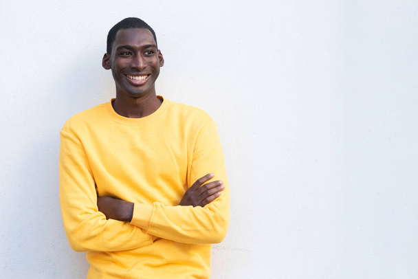 Portret lachende jonge zwarte man met armen gekruist door witte muur - Foto, afbeelding