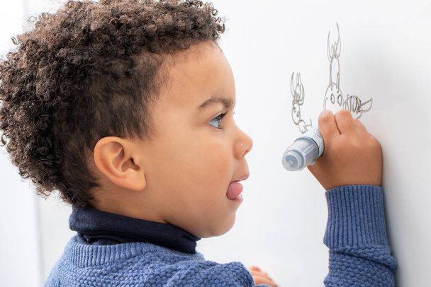 Zamknij się portret małego afro amerykański chłopiec rysunek z markerem długopis na białej tablicy. - Zdjęcie, obraz