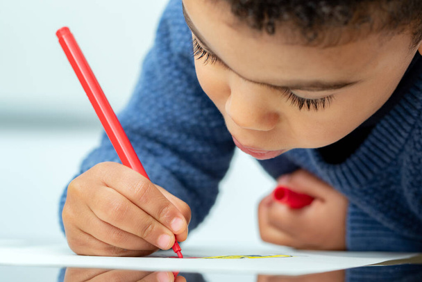 Extremo primer plano del pequeño niño afroamericano dibujando con rotulador. - Foto, Imagen