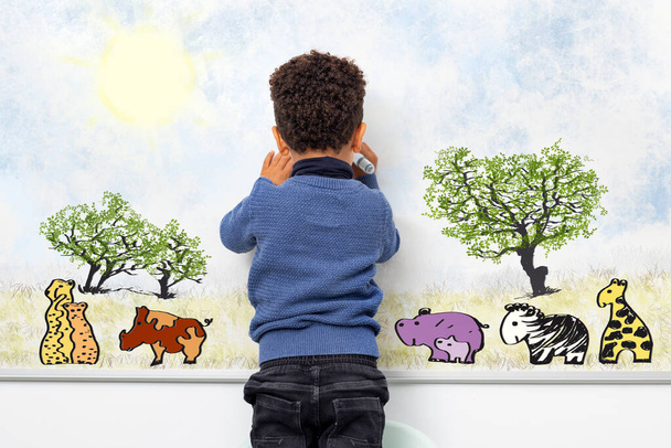 Közepes közelkép visszapillantás portré afro-amerikai gyerek rajz állatok fehér táblára. Gepárd, varacskos disznó, víziló, zsiráf, zebra és fák.  - Fotó, kép