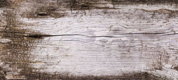 Superficie de un viejo tablón de madera áspero trabajado cubierto de grietas y en ruinas alrededor de los bordes, vista panorámica, textura, fondo - Foto, imagen
