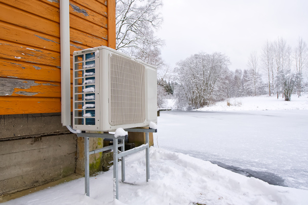 Luft-Wasser Wärmepumpe in der Nähe eines alten Holzhauses im Winter. Luft-Wasser-Wärmepumpe, emissionsarme erneuerbare Energien aus nächster Nähe - Foto, Bild