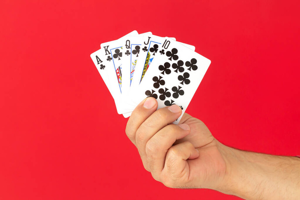 Mužská ruka drží kombinaci královské flush pokerové karty na červeném pozadí. Kasino štěstí koncept štěstí - Fotografie, Obrázek