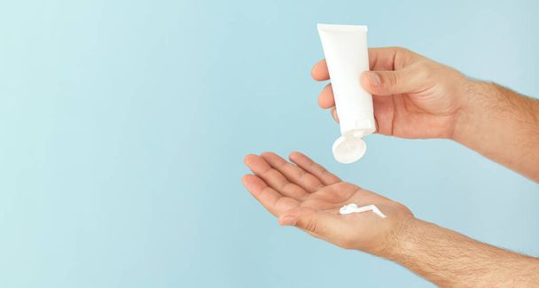 Las manos masculinas aplican crema hidratante cosmética para el cuidado de la piel sobre fondo azul claro con espacio para copiar - Foto, imagen