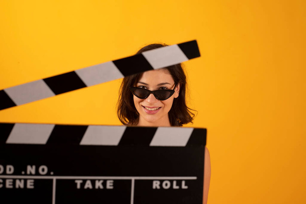 woman with popcorn glasses and clapperboard cinema, yellow background - Photo, Image