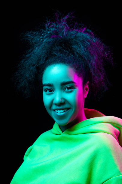 African-american womans portrait isolated on dark studio background in multicolored neon light - 写真・画像