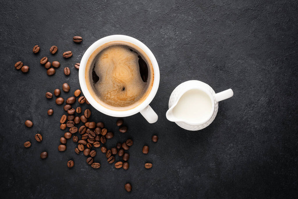 Cup of black coffee and coffee creamer in a jug on black concrete background, top view - Foto, immagini