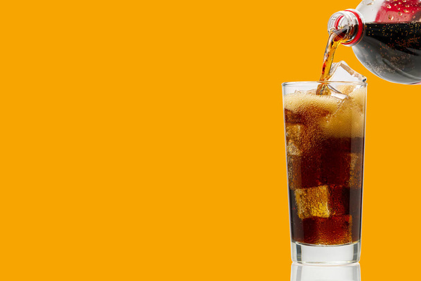 Cola gieten op glas met ijsblokjes geïsoleerd op oranje, kopieer ruimte - Foto, afbeelding