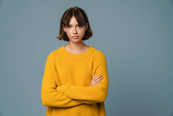 Portrait of an upset young casual girl standing with arms folded isolated over blue background - Foto, afbeelding