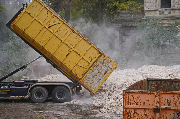 Ciężarówka na placu budowy podnosząca kontener i wysypująca gruz budynku - Zdjęcie, obraz
