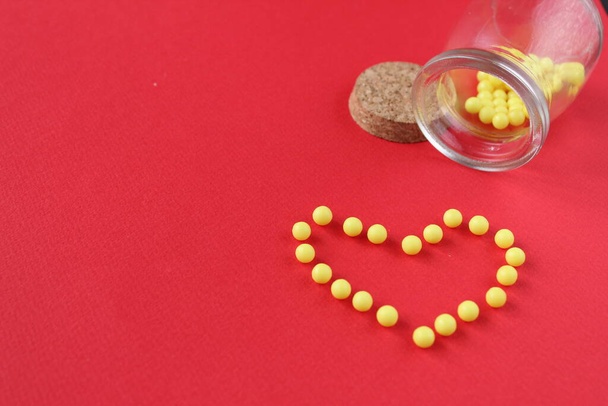 Βιταμίνες δισκίο ομοιοπαθητική χύνεται από βάζα βρίσκονται καρδιά σε κόκκινο φόντο με ένα αντίγραφο του χώρου για το κείμενο - Φωτογραφία, εικόνα