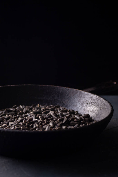sunflower seeds in a black charred cast iron skillet on a gray concrete table in a dark key, rustic - Фото, изображение
