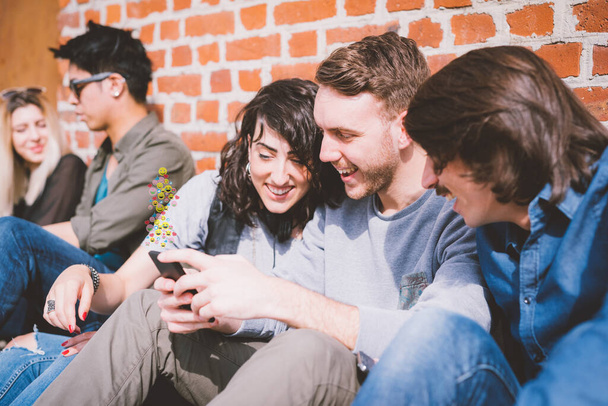 Grupo de amigos multiétnicos millennials usando smartphone viciado em tendências de tecnologia seguindo e conversando usando emoji e emoticon  - Foto, Imagem