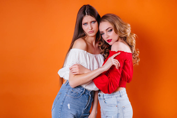 Two young and beautiful girls shows emotions and smiles in the Studio on an orange background. Girls for advertising - Foto, afbeelding