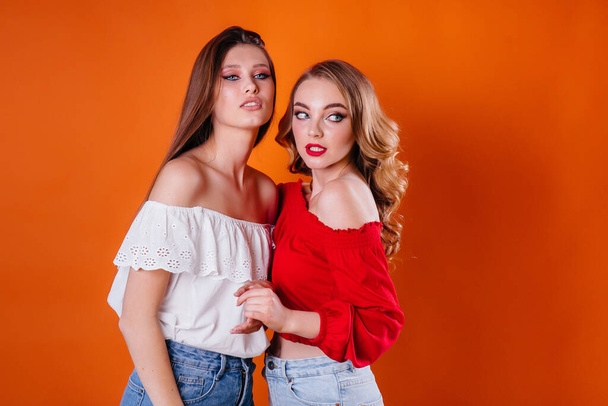 Two young and beautiful girls shows emotions and smiles in the Studio on an orange background. Girls for advertising - 写真・画像