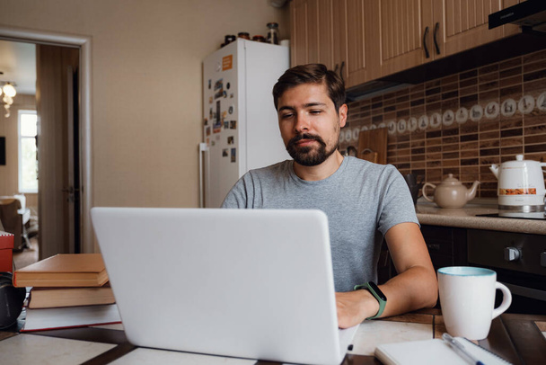 young man freelancer using laptop studying online or working from home, happy casual millennial guy typing on pc notebook surfing internet looking at screen enjoying distant job sit at table - Photo, image