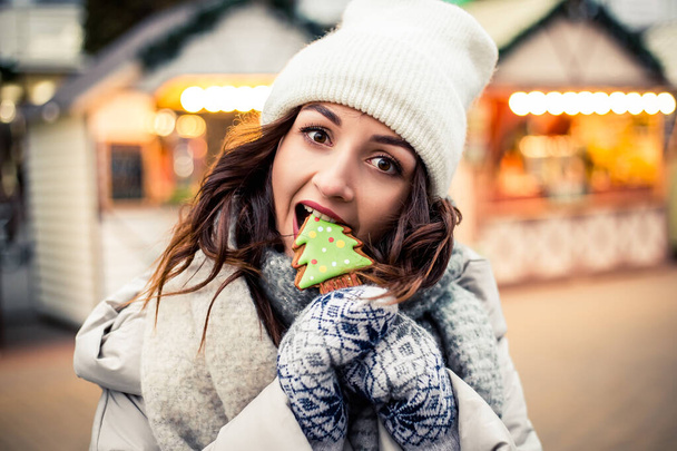 若い美しい女性が街の棒にジンジャーブレッドキャンディーチョコレートクッキーを食べ立って、かわいい空腹甘い歯。新年のクリスマスの装飾、バレンタインデーのコンセプト. - 写真・画像