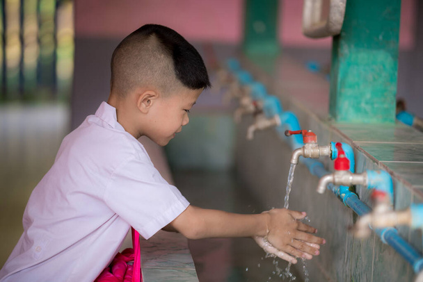 Un bambino asiatico che si lava le mani a scuola. Un lavandino combinato che può lavare più persone contemporaneamente. Pulizia per proteggere batteri e virus nel corpo. Per una buona salute, anti-sporco. - Foto, immagini