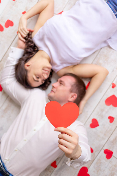 día de San Valentín, una pareja enamorada yace entre los corazones en el suelo abrazando y sosteniendo un gran corazón rojo - Foto, imagen