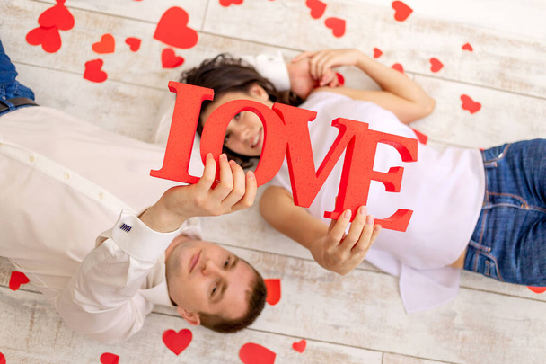 День валентина, закохана пара лежить серед сердець на підлозі і тримає великий напис Любов
 - Фото, зображення