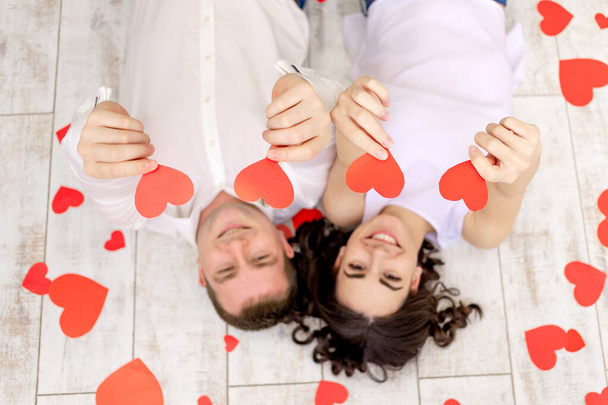 Ημέρα του Αγίου Βαλεντίνου, ένα ερωτευμένο ζευγάρι βρίσκεται ανάμεσα στις καρδιές στο πάτωμα κρατώντας καρδιές στα χέρια τους - Φωτογραφία, εικόνα