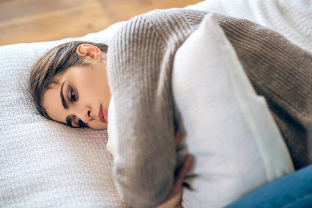 Dark-haired young woman lying hugging her pillow and looking lonesome - Foto, immagini