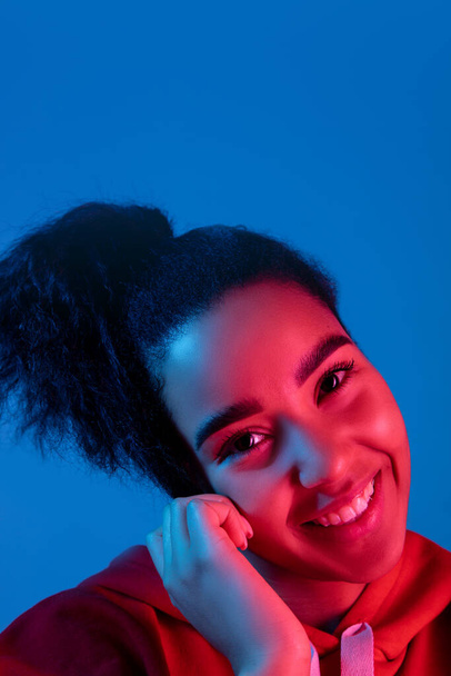 African-american womans portrait isolated on blue studio background in multicolored neon light - Fotoğraf, Görsel