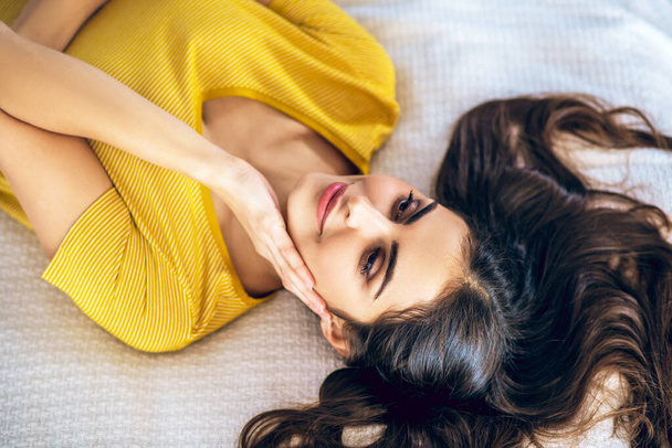 Dlouhovlasá krásná mladá žena ležící na posteli a vypadá uvolněně - Fotografie, Obrázek