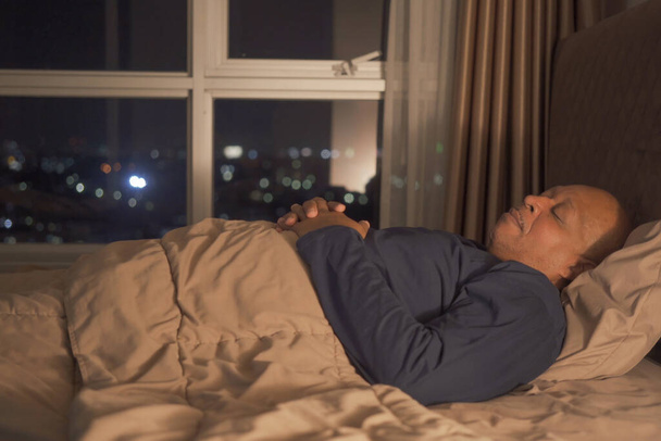 Schläfriger alter schwarzer Mann gähnt. Afroamerikaner liegen und schlafen zu später Stunde zu Hause auf dem Bett im Schlafzimmer. Lebensstil - Foto, Bild