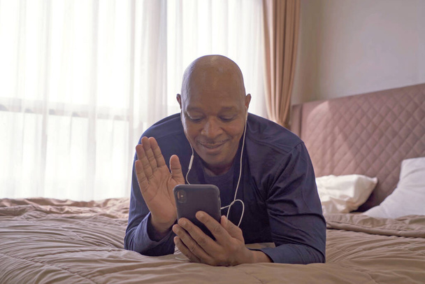 Feliz negócio sorridente, homem negro, afro-americanos falando ao telefone com colegas na videoconferência da webcam em quarentena na cama no quarto em casa de manhã. Estilo de vida - Foto, Imagem