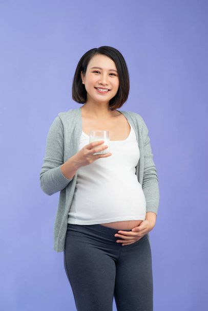Young pregnant woman with glass of milk over purple background - Фото, изображение