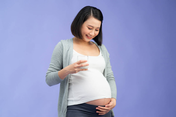 Zwangerschap en calcium. gelukkig zwanger vrouw holding glas van melk glimlachen op camera staande over kleur achtergrond - Foto, afbeelding