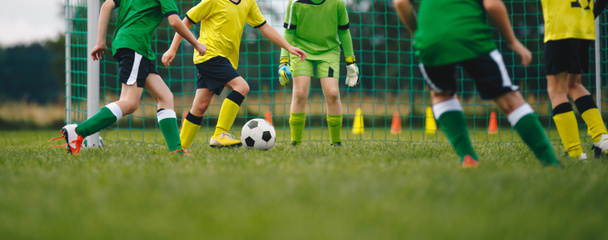 Οριζόντια εικόνα των παιδιών που παίζουν ποδόσφαιρο. Ευτυχισμένα αγόρια κλωτσάνε κλασσική μπάλα ποδοσφαίρου στο γρασίδι. Τα παιδιά των σχολείων ανταγωνίζονται σε αθλητικό παιχνίδι σε αγωνιστικό γήπεδο - Φωτογραφία, εικόνα