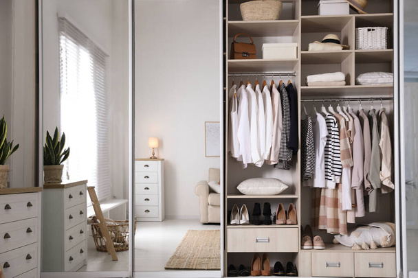 Armario armario con diferentes ropa elegante, zapatos y cosas del hogar en la habitación - Foto, Imagen