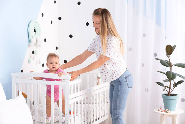 Mother with cute baby standing in crib at home - Foto, imagen